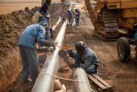 Workers wearing protective clothing fixing welding and grinding industrial construction oil and gas pipeline.
